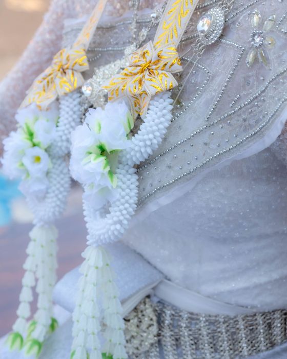 พวงมาลัยดอกไม้สีขาวประดับริบบิ้นสีทองบนชุดไทยสีขาว